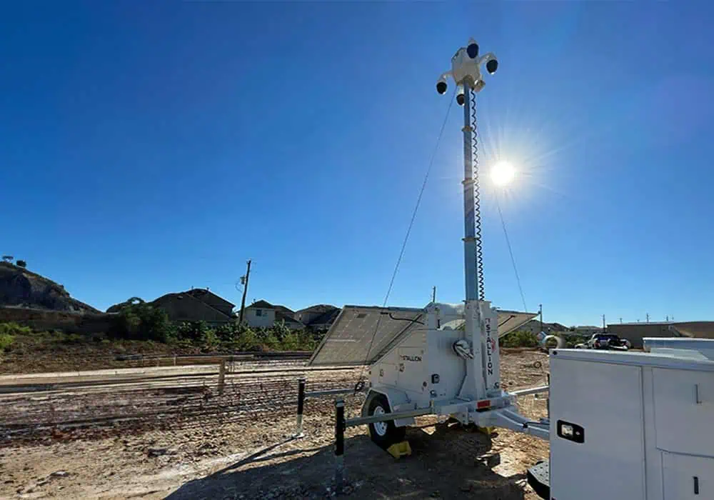 A mobile surveillance trailer with solar security camera and panels provides parking lot and construction site video security under a blue sky.