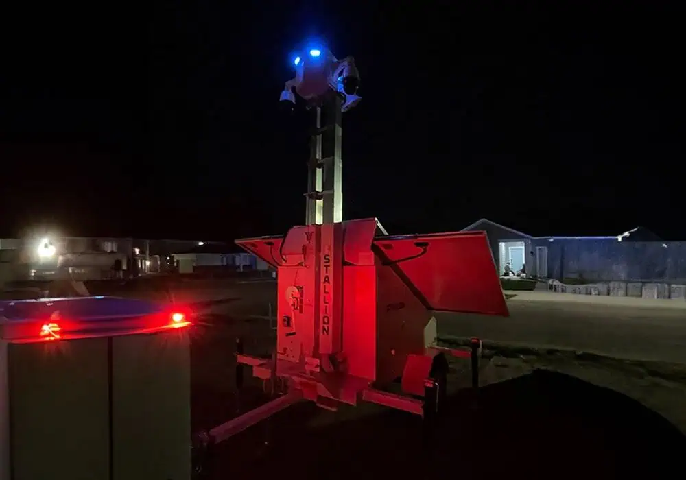 A mobile surveillance trailer with solar security cameras and blue lights ensures commercial video security in a parking lot at night.