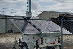 A mobile surveillance trailer with solar security cameras stands behind a chain-link fence, providing mobile video security for parking lot and commercial security systems.