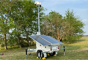 A mobile surveillance trailer with solar security cameras on grass showcases parking lot security and commercial security systems in outdoor areas.