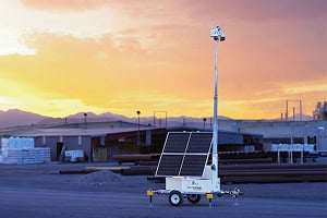 A mobile surveillance trailer with solar security camera stands in a parking lot at sunset, showcasing commercial security systems.