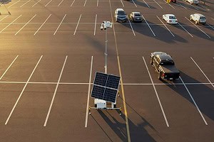 A mostly empty parking lot with a mobile surveillance trailer and solar security camera for commercial parking lot security.