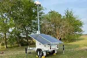 A solar-powered mobile surveillance trailer with a telescoping security camera mast provides commercial parking lot video security.