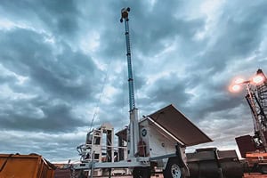 A mobile surveillance trailer with solar security camera and mast for commercial parking lot security is outdoors under cloudy skies.