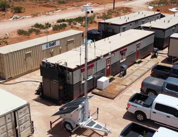 A mobile surveillance trailer with solar security cameras provides parking lot and construction site video security near office trailers and trucks.